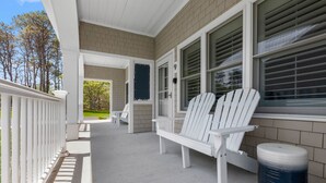 A covered porch with white Adirondack chairs, a trash can, and a door marked with the number 9. - Pelham on Earle (West Harwich)