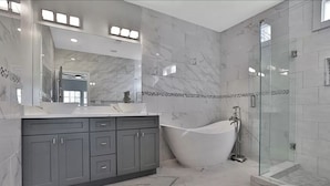 A modern bathroom with a freestanding bathtub, a glass-enclosed shower, and a large vanity with a mirror.