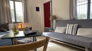 Et hyggeligt værelse med en sofa, et spisebord og en stol. Der er en lampe på bordet og en flaske på bordet.