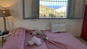 Et soveværelse med seng, lampe, vindue med havudsigt og et rødt skab.