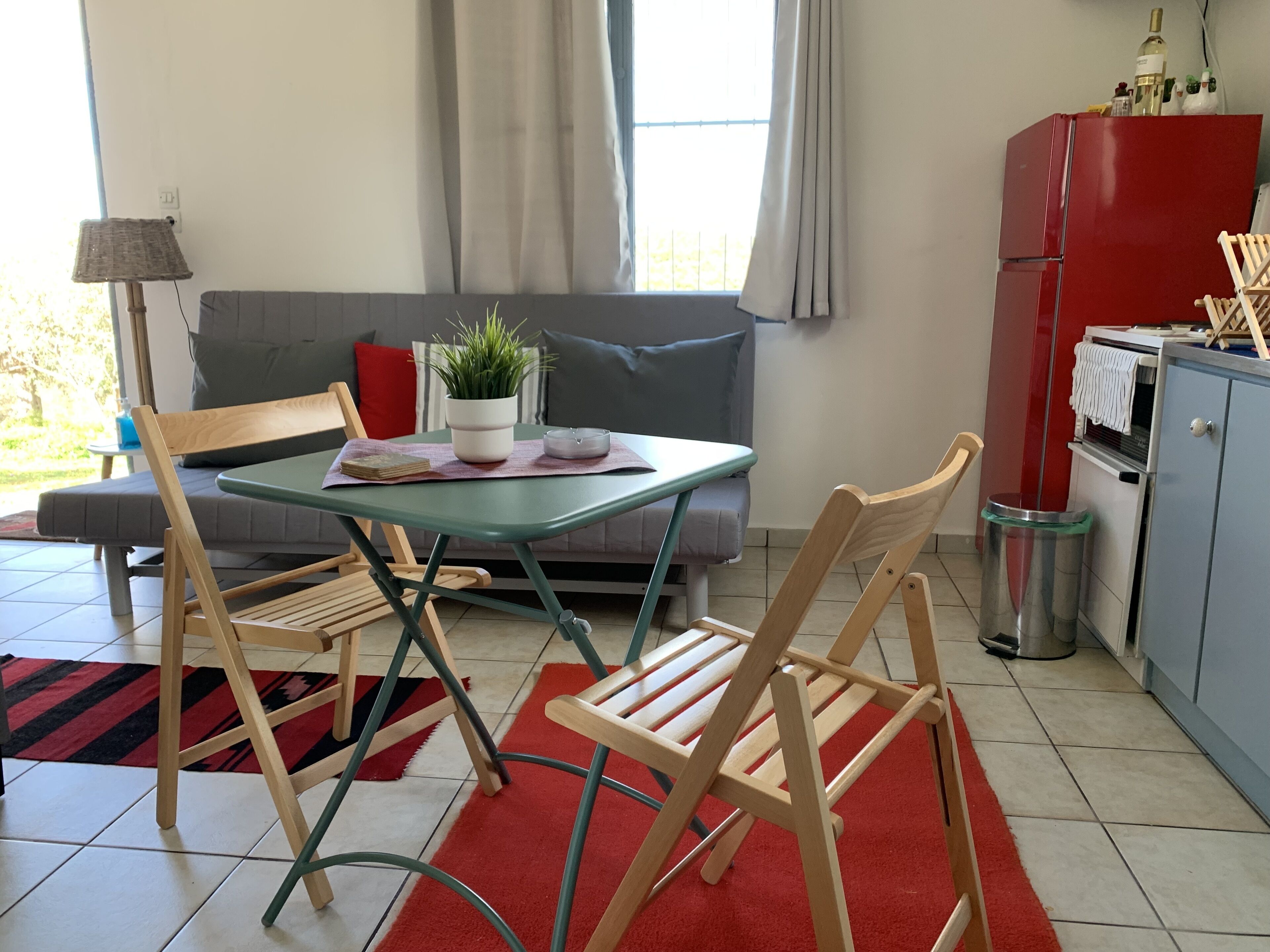 Een moderne woonkamer met een bank, een eettafel met stoelen, een potplant en een rode koelkast.