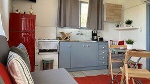 Et kompakt køkken med et rødt køleskab, grå skabe og et lille spiseområde med et klapbord og stole.