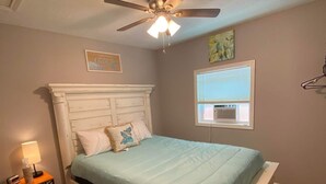 Un dormitorio con cama, ventilador de techo, mesita de noche y ventana con persianas.