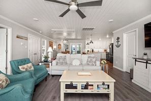 A modern living room with a teal sofa, a white coffee table, and a ceiling fan.