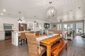 A spacious kitchen with a large island, wooden dining table, and wicker chairs.