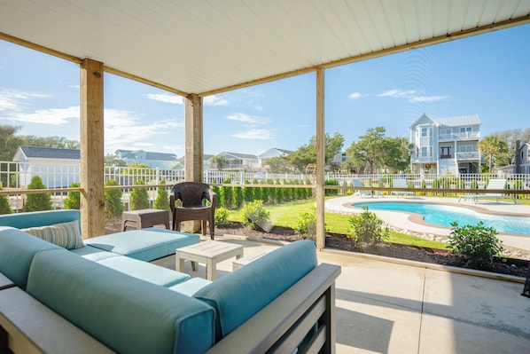 A covered outdoor seating area with a pool view, wooden deck, and a view of neighboring houses.