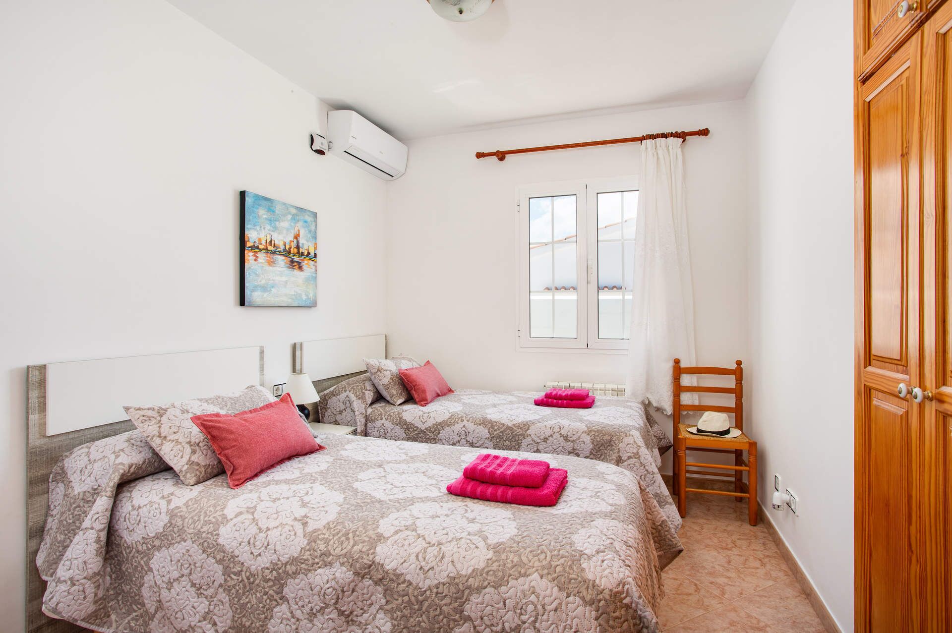 Quarto com duas camas, janela com cortinas, radiador e uma cadeira de madeira.