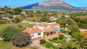 Une villa blanche avec un toit recouvert de tuiles rouges, une piscine et une vue sur une montagne.