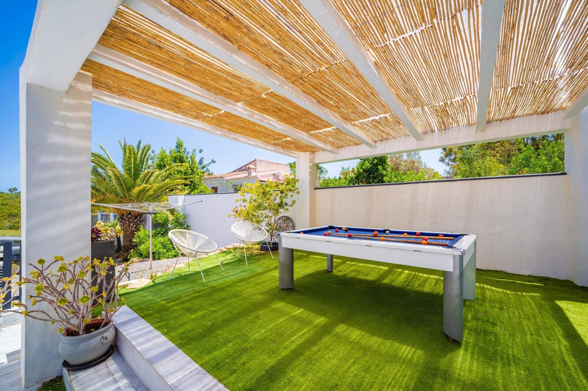 An outdoor pool table with a clear view of the surrounding greenery and a white wall.