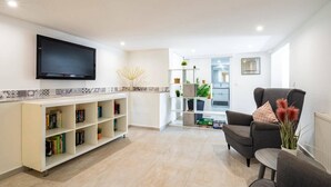 A modern living room with a flat-screen TV, a bookshelf, a grey armchair, and a small table with a vase of plants. - Villa Tomillo by Villa Plus (Jávea)