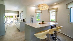 A modern kitchen with a central island, bar stools, and pendant lighting. - Villa Tomillo by Villa Plus (Jávea)