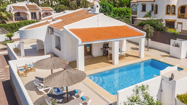 Un espace piscine aménagé sur le toit, avec des chaises longues et des parasols, entouré de bâtiments blancs aux toits recouverts de tuiles orange.