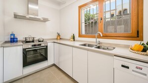 Une cuisine moderne avec des armoires blanches, une cuisinière en acier inoxydable, un four, un lave-vaisselle et une fenêtre donnant sur un jardin.