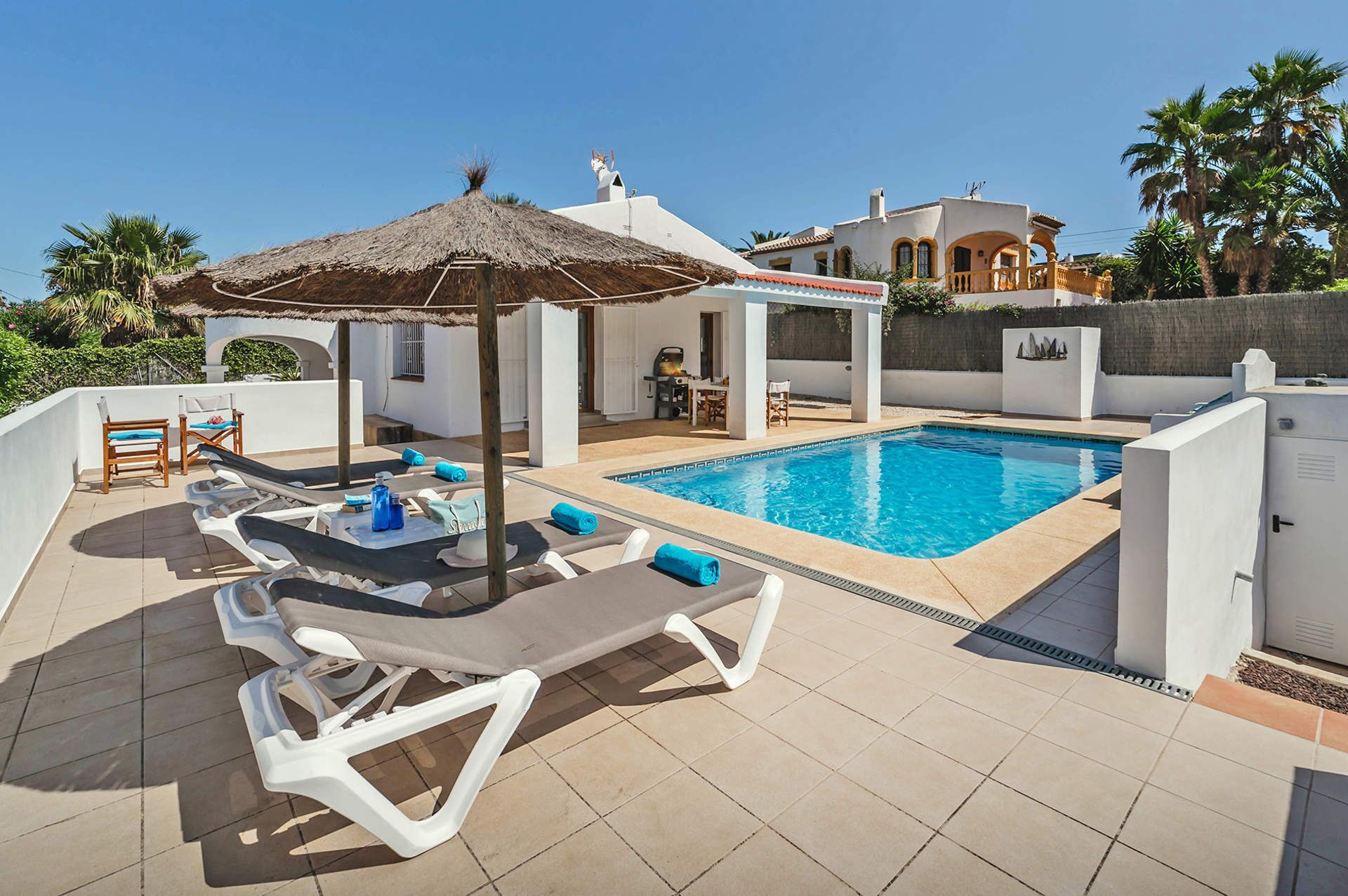 A poolside area with lounge chairs, a thatched umbrella, and a view of a white building with arches.