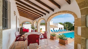 Une terrasse couverte avec une piscine, des chaises rouges et une table.