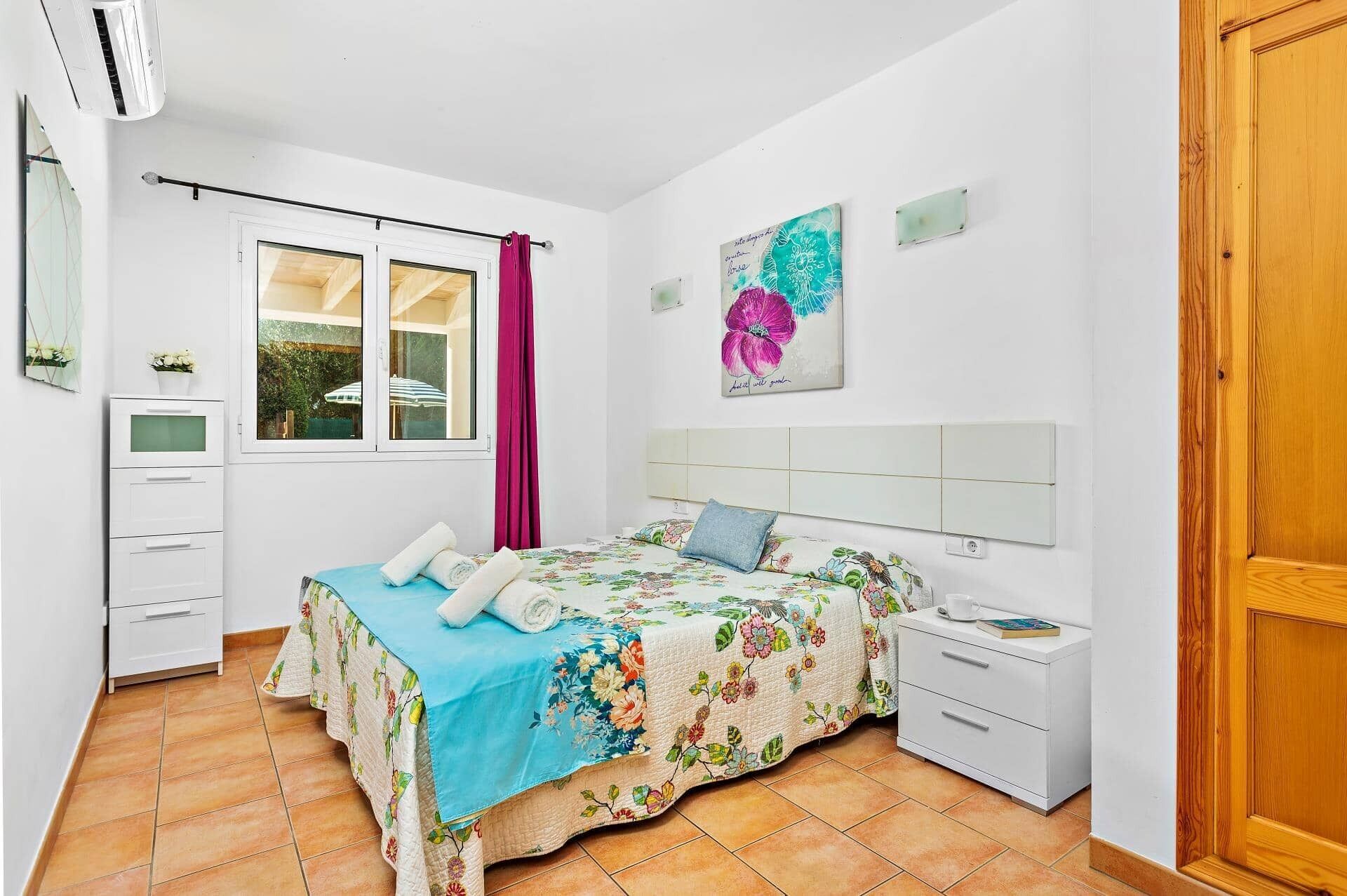 A bedroom with a bed, a nightstand, a dresser, a window with curtains, and a door.