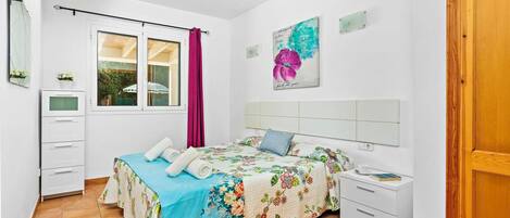 A bedroom with a bed, a nightstand, a dresser, a window with curtains, and a door.