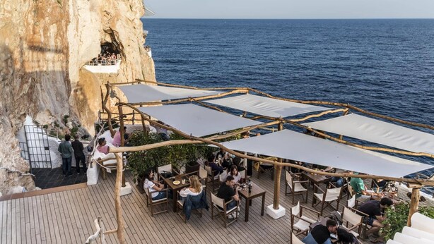 Un espace extérieur aménagé avec des tables et des chaises, offrant une vue sur une falaise et la mer.