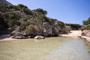 A coastal area with clear shallow waters, rocky cliffs, and a sandy beach.