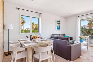 A dining area with a table set for four, a sofa, and a view of the outdoors. - Villa Natasha by Villa Plus (Los Delfines)