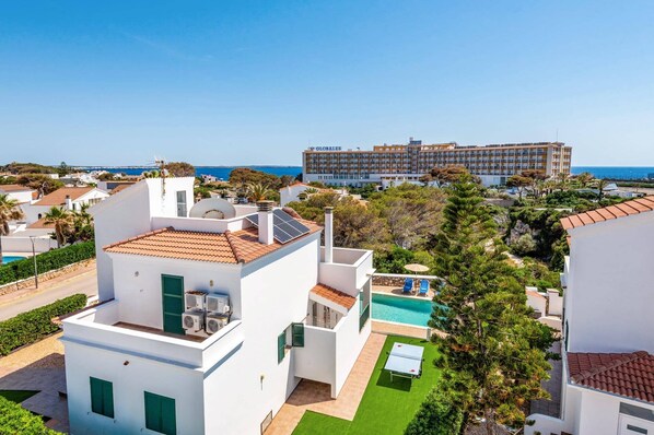 Zona residencial con piscina, paneles solares y un gran hotel al fondo.