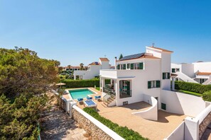 A modern villa with a swimming pool, outdoor seating, and a view of neighboring houses.