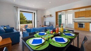 A modern living room with a blue sofa, a dining table set for four with blue napkins, and a kitchen visible through an open door.