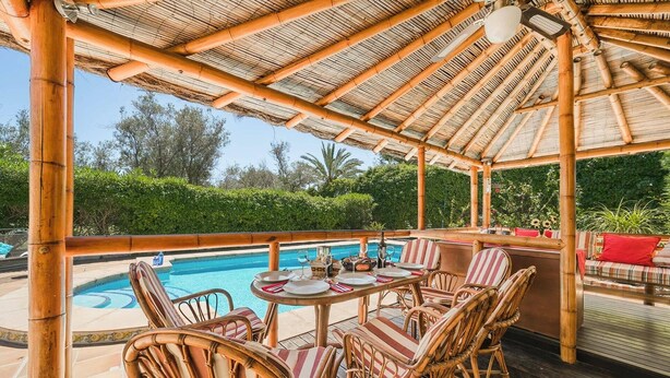 Un espace piscine extérieur aménagé avec du mobilier en bambou et doté d’un toit de chaume.