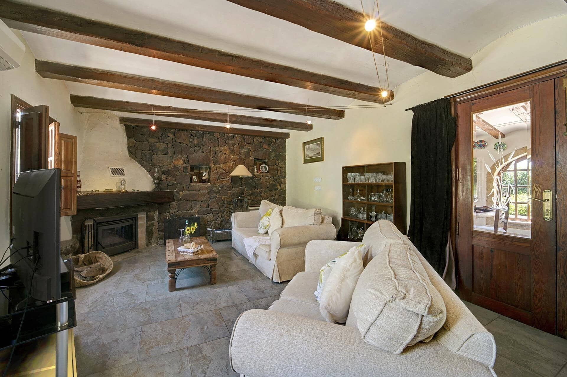 Ein Wohnzimmer mit Kamin aus Stein, Holzbalken, einer Couch und einem Fernseher.