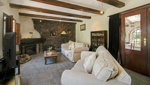 Un salon avec une cheminée en pierre, des poutres apparentes, un canapé et un téléviseur.