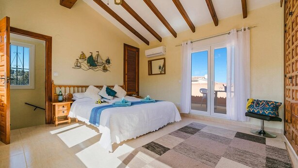 A bedroom with a bed, a nightstand, a window, a door, and a view of the outside. - Villa Toscamar by Villa Plus (El Tosalet)