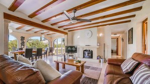 A spacious living area with a fireplace, leather sofas, a dining area with a table and chairs, and a large TV. - Villa Toscamar by Villa Plus (El Tosalet)
