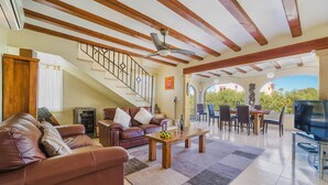 A spacious living area with a staircase, leather sofas, a dining table, and a TV. - Villa Toscamar by Villa Plus (El Tosalet)