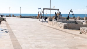 Un camino pavimentado con columpios y un muro de piedra, que lleva a una masa de agua.
