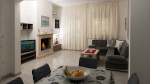 Una sala de estar con televisión, chimenea, sofá y una mesa de comedor con un tazón de fruta.