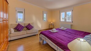 A bedroom with a bed, a sofa, a nightstand, and a window.