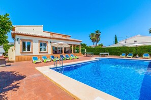 Uma área de piscina com espreguiçadeiras, um espaço de estar coberto e um edifício com telhado de azulejos.