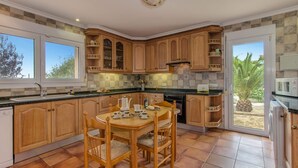 A kitchen with wooden cabinets, a dining table with chairs, and a view of palm trees outside.