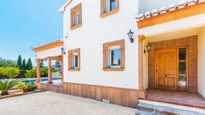 A two-story building with a white facade, a wooden door, and a covered patio area with a pool.