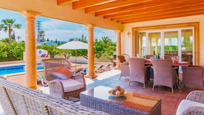 A covered outdoor area with wicker furniture, a pool, and a dining table with chairs.