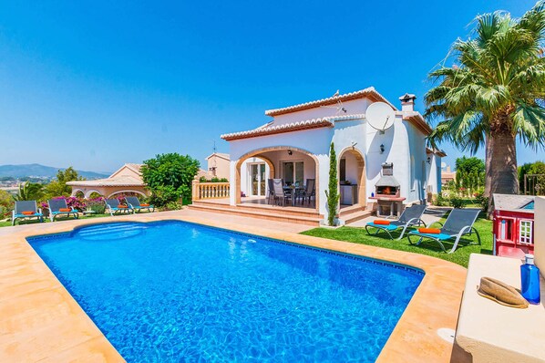 A swimming pool with a patio area, a small building with a chimney, and a view of the landscape.