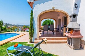 A poolside area with a barbecue grill, outdoor seating, and a view of the landscape.