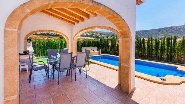 Ein überdachter Außenbereich mit Pool, Sitzgelegenheiten und Blick auf die Landschaft.