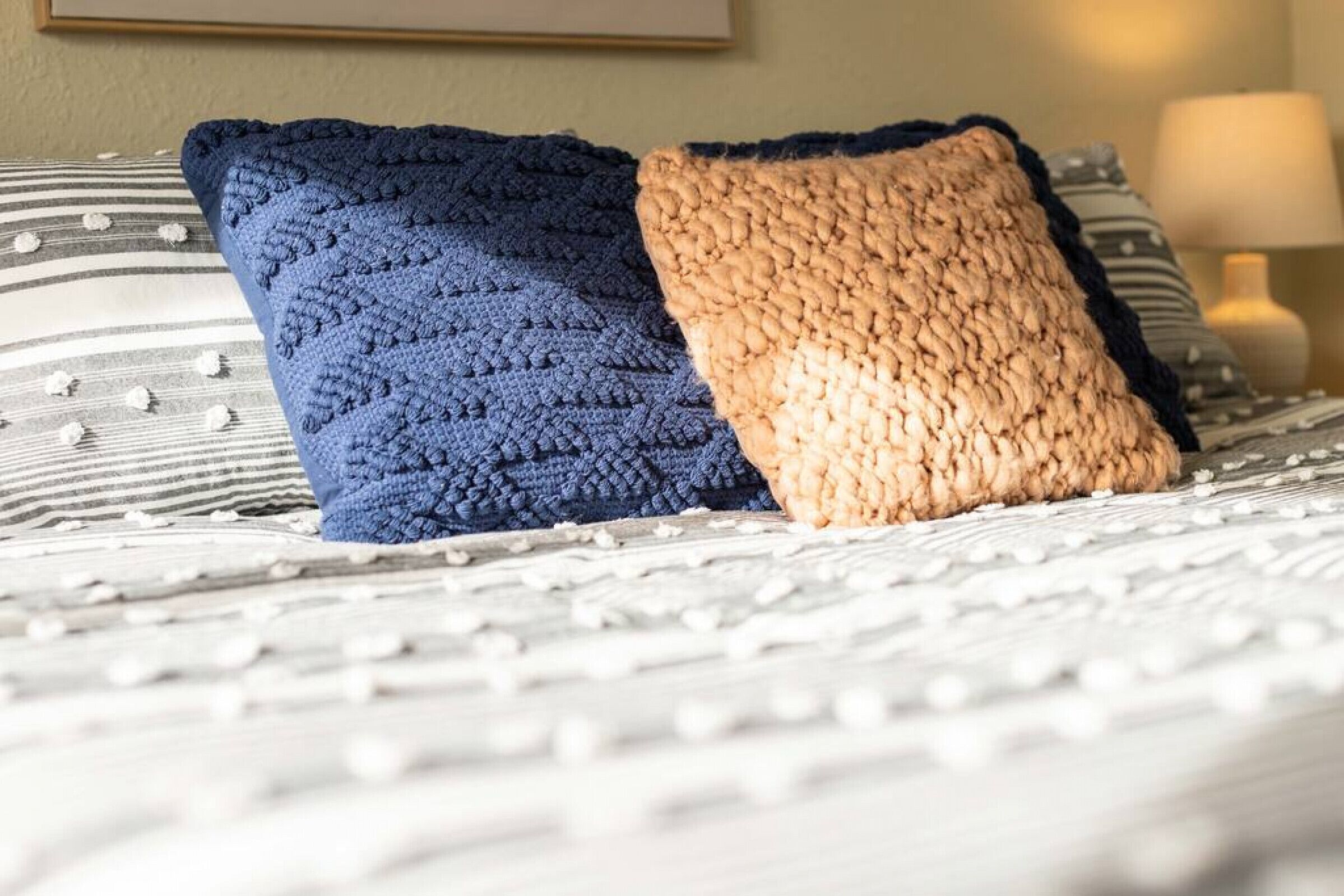 A bed with two pillows, one blue and one beige, on a striped bedspread.