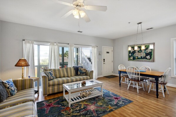 A spacious living room with a ceiling fan, a striped sofa, a coffee table, and a dining table with chairs.