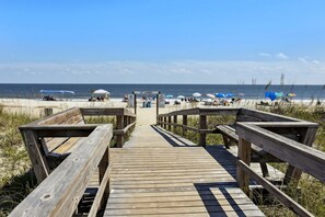 A wooden boardwalk leading to beach umbrellas and beachgoers.