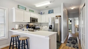Uma cozinha moderna com armários brancos, uma ilha central com banquetas, geladeira e micro-ondas.