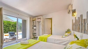 A hotel room with two beds, a sliding glass door to a balcony, a wooden wardrobe, and a wall-mounted light fixture. - Villa Jessie by Villa Plus (Montgo de Toscamar)