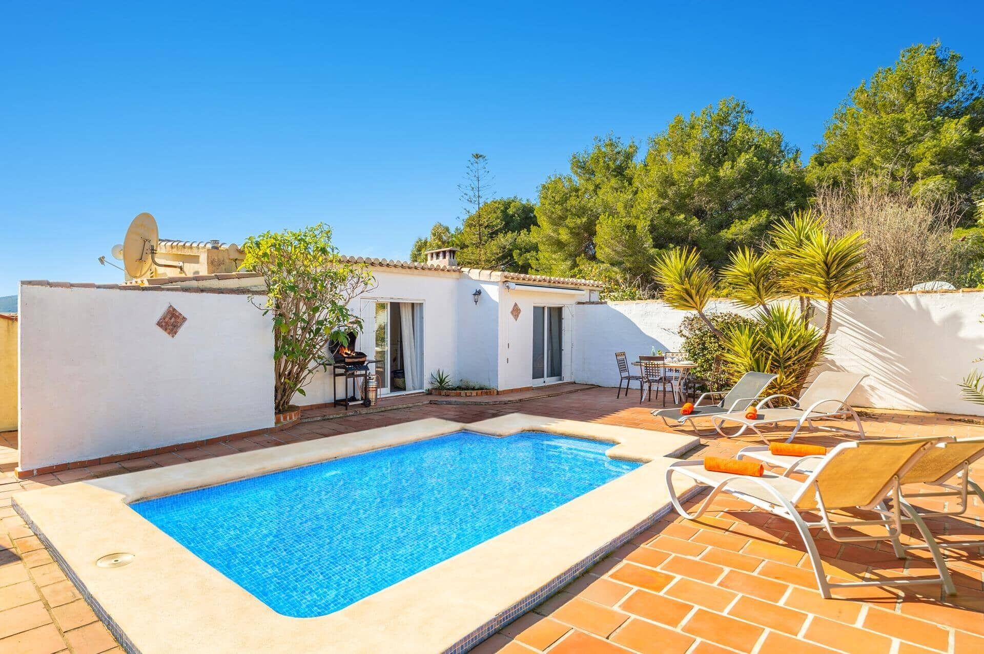 A swimming pool with lounge chairs, a barbecue area, and a small patio with a table and chairs.