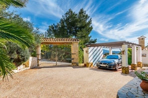 A gated entrance with a gravel driveway leading to a covered car parking area.